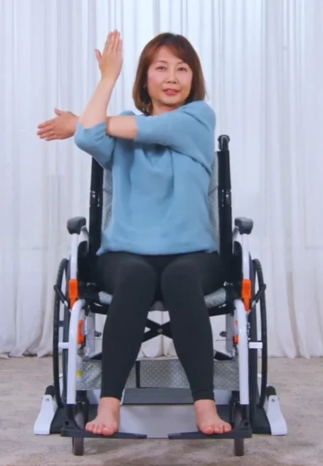 手動の車椅子に座ったまま、TPA-02に乗っている女性。車輪は台の両側、足は中央の台に乗せている